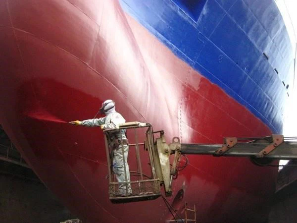 Marine Coating Pekerja sedang mengaplikasikan cat antifouling pada lambung kapal besar menggunakan alat semprot di galangan kapal