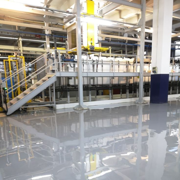 cat epoxy tahan panas Lantai pabrik industri dengan lapisan cat epoxy mengkilap, mencerminkan mesin dan struktur logam di sekitarnya.