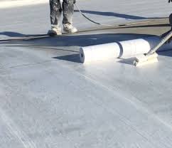 Pekerja mengaplikasikan pelapis bangunan dengan cat coating cepat kering menggunakan roller pada permukaan lantai saat musim kemarau.