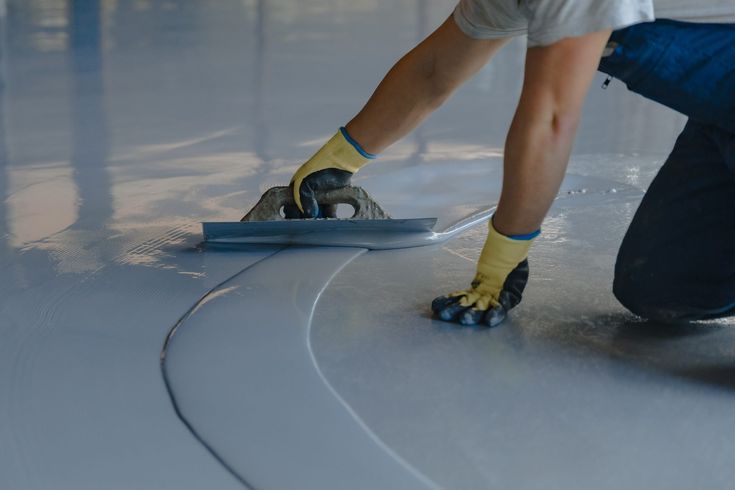 Pekerja mengaplikasikan floor coating atau cat coating cepat kering pada permukaan lantai bangunan industri sebagai pelapis bangunan tahan lama.